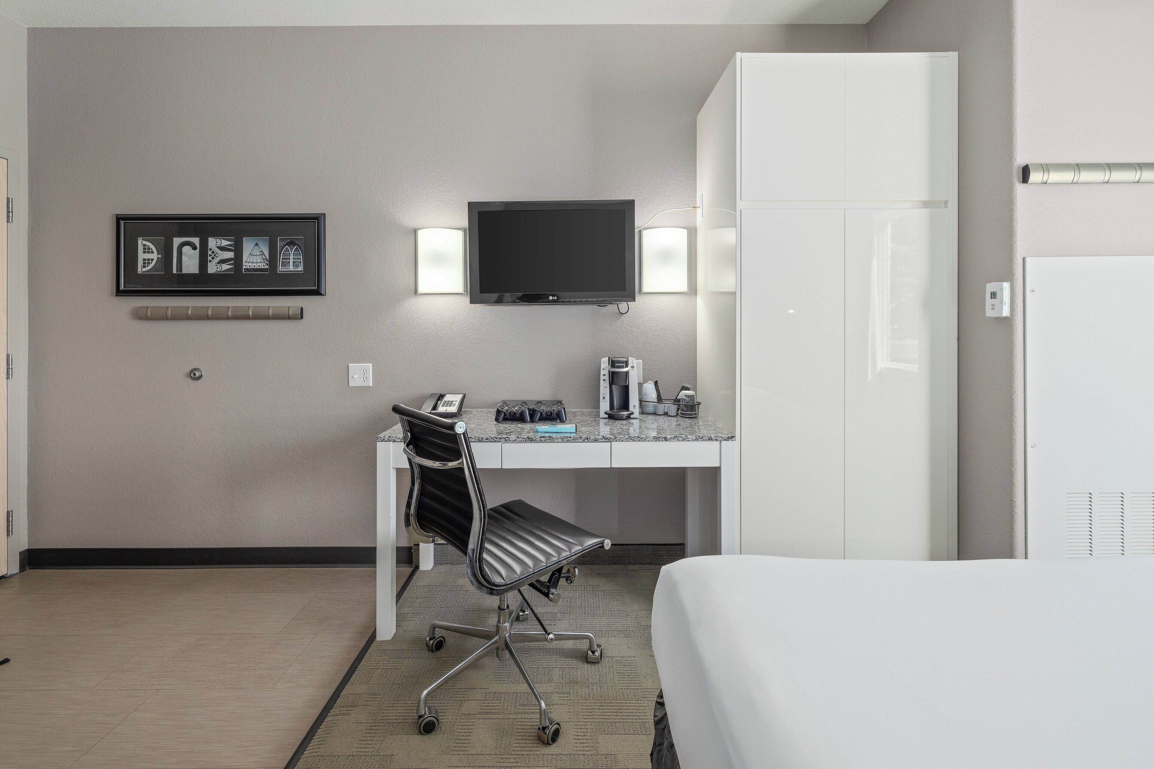 Una habitación de hotel con cama, escritorio y silla, televisión y un cuadro en la pared.