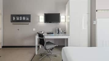 Una habitación de hotel con cama, escritorio y silla, televisión y un cuadro en la pared.