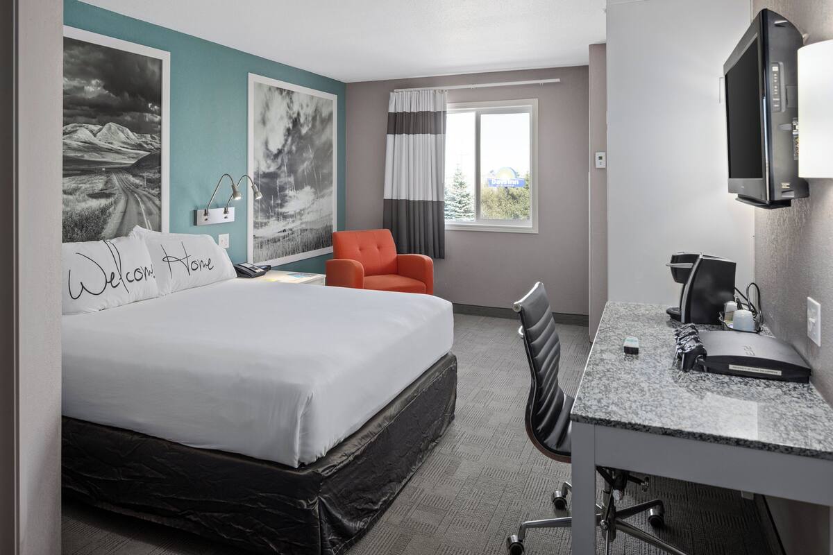 Une chambre d’hôtel équipée d’un lit, d’un bureau, d’une chaise, d’une télévision et décorée avec des œuvres d’art.