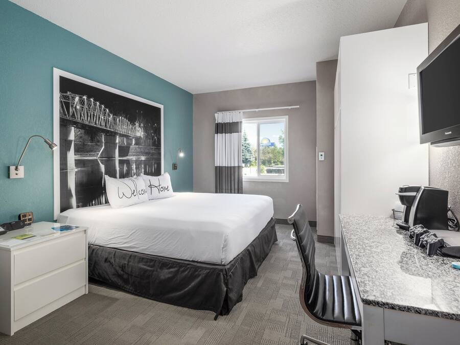 Une chambre d’hôtel avec un lit, un bureau, une télévision et une fenêtre avec des rideaux.