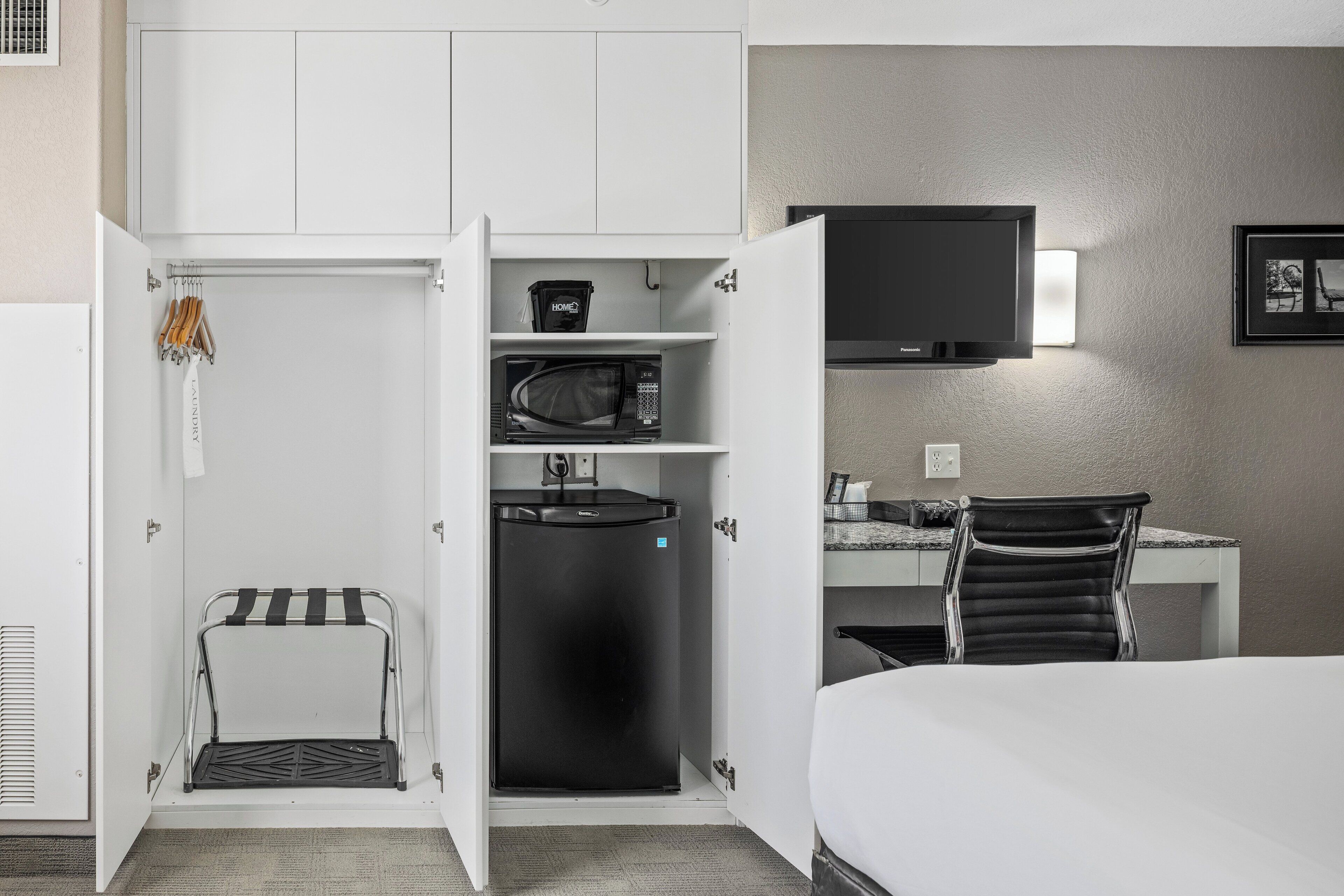 A compact hotel room with a bed, a desk with a chair, a television, a microwave, and a mini-fridge.