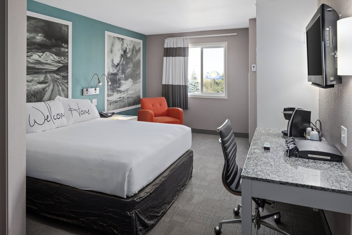 A hotel room with a bed, a desk, a chair, a TV, and artwork on the walls.