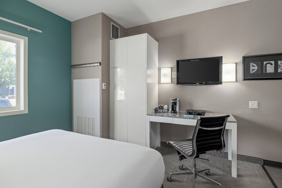 A hotel room with a bed, a desk with a chair, a television, and a window.