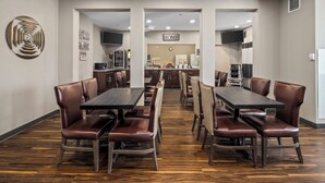 A dining area with a central table, multiple chairs, a kitchen area, and a 'HOME' sign. - Prairie Crest Medicine Hat (Medicine Hat)