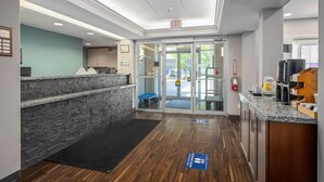 A reception area with a stone wall, a reception desk, a glass door entrance, and a coffee station. - Prairie Crest Medicine Hat (Medicine Hat)
