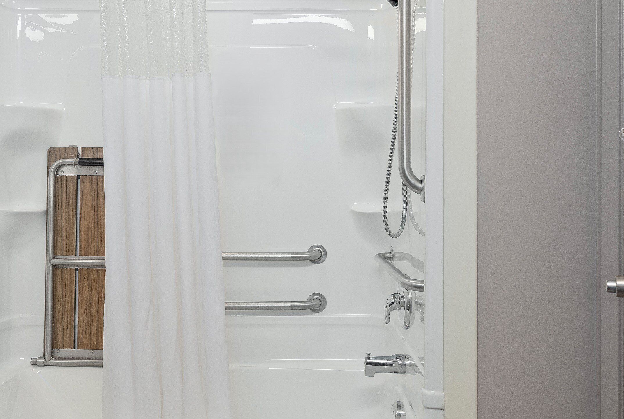 Un baño con ducha, barras de apoyo y panel de madera.