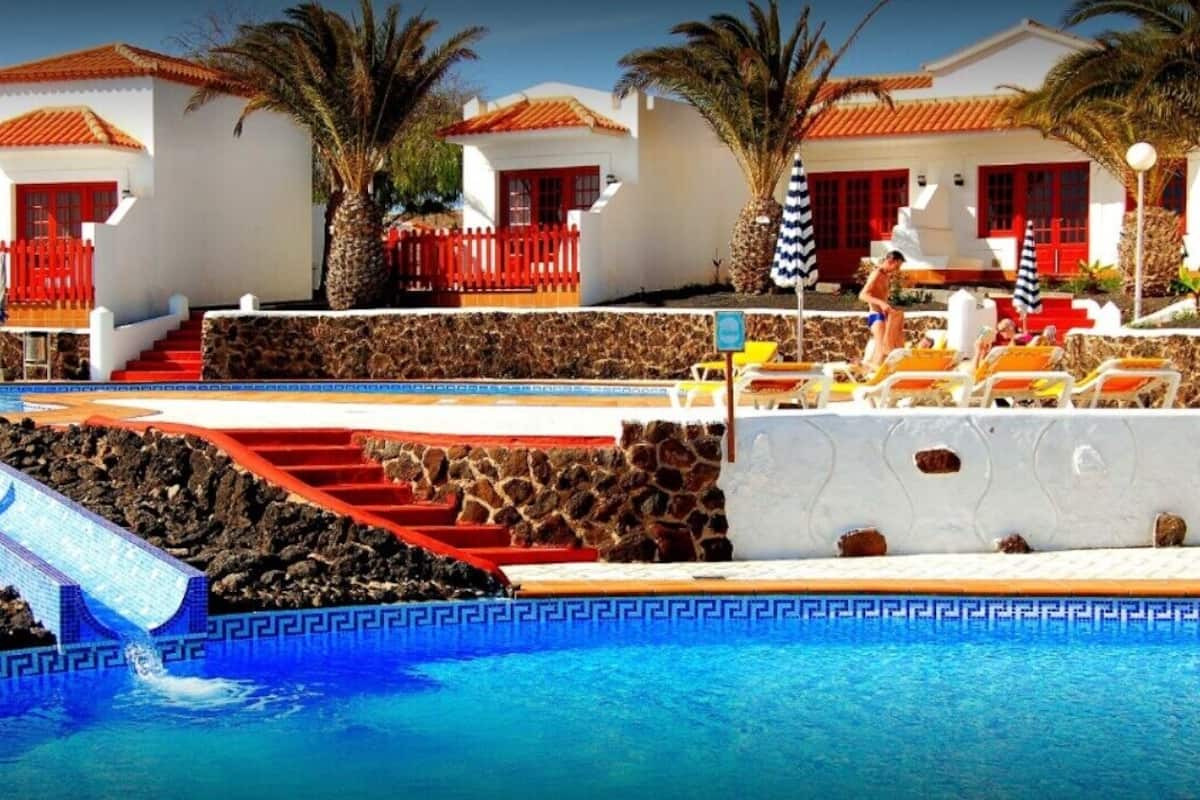 A pool area with a stone wall, red steps, and lounge chairs.