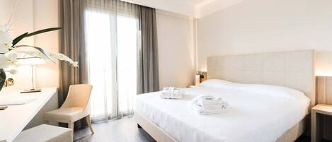 A hotel room with a bed, a desk, a chair, and a lamp.