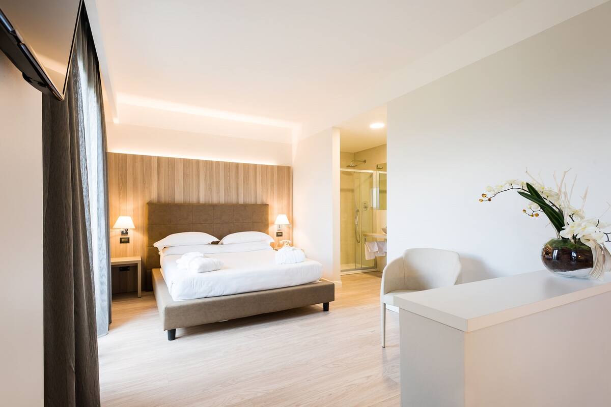 A modern hotel room with a large bed, bedside lamps, a shower area, and a reception desk.