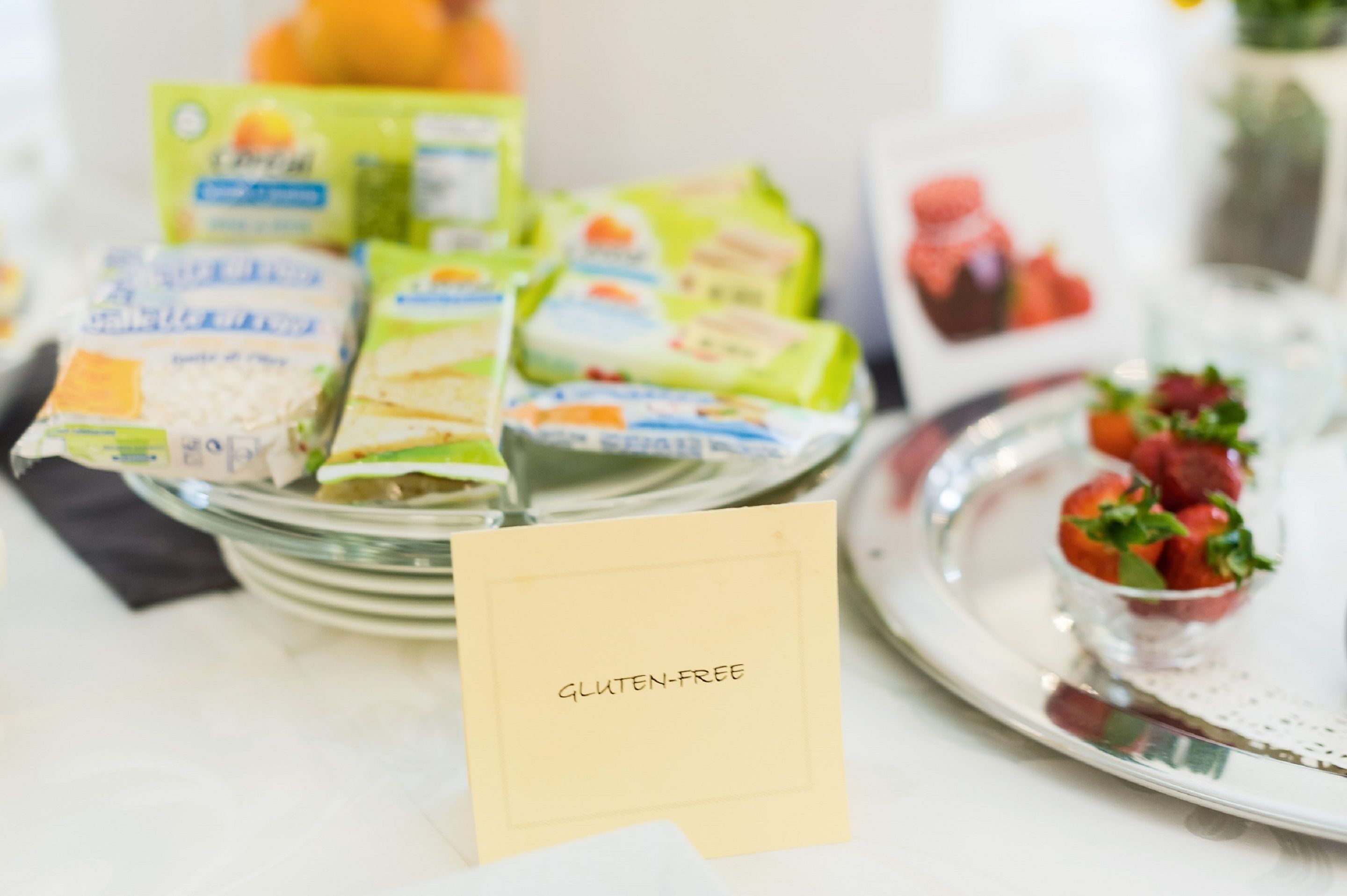Una mesa de buffet con productos etiquetados como sin gluten y un cuenco pequeño de fresas.