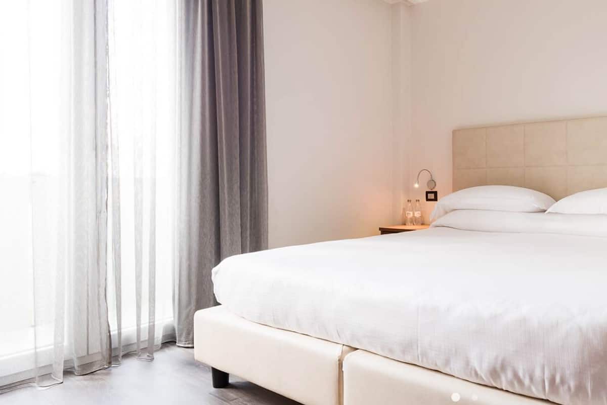 A hotel room with a bed, a nightstand, a lamp, and a window with curtains.