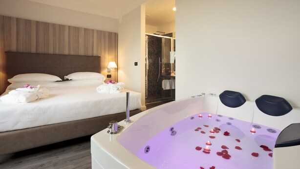 A hotel room with a large bed, a separate bathroom with a shower, and a jacuzzi with rose petals.