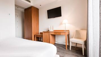 Una habitación de hotel con una cama, un escritorio de madera, una silla, un televisor y una lámpara.