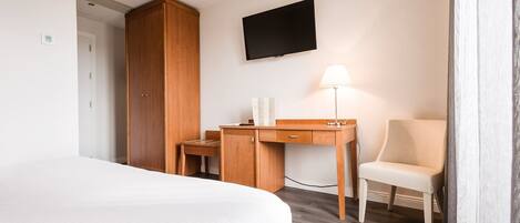 A hotel room with a bed, a wooden desk, a chair, a TV, and a lamp.