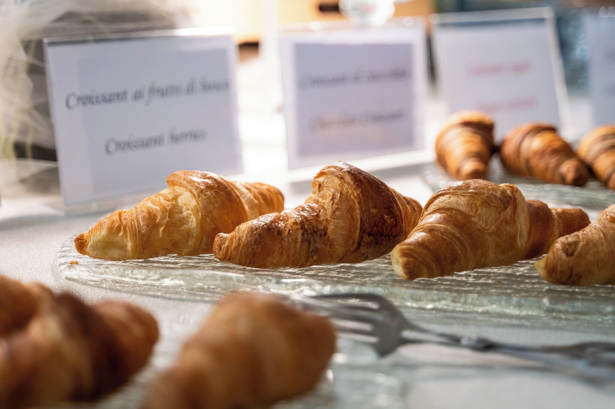 Een presentatie van croissants op een glazen bord met labels die verschillende soorten aanduiden.