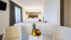 A hotel room with a bed, bedside tables, a TV, and a fruit bowl on a table.