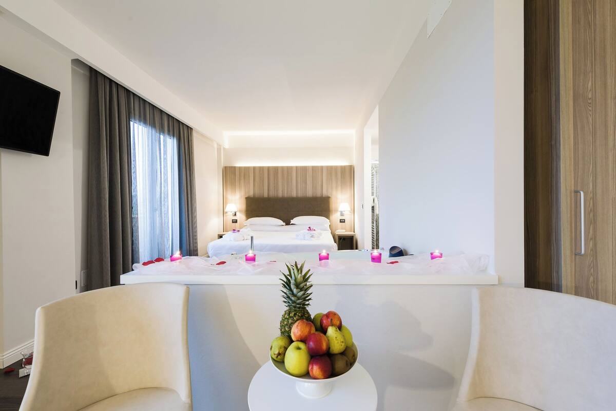 A hotel room with a bed, bedside tables, a TV, and a fruit bowl on a table.
