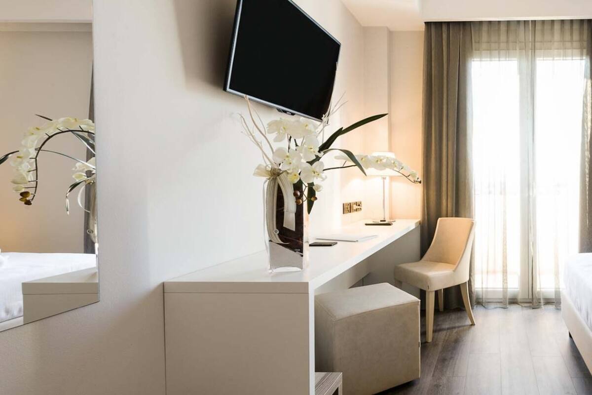 A hotel room with a bed, a desk, a chair, a TV, and a window with curtains.