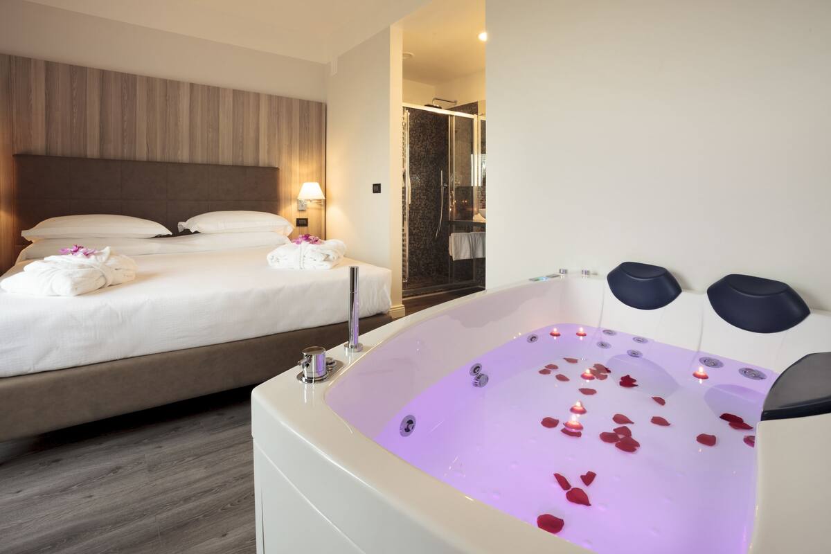 A hotel room with a large bed, a bathtub with rose petals, and a shower area.