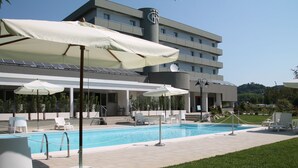 A modern hotel with a swimming pool, outdoor seating, and a view of a hill.
