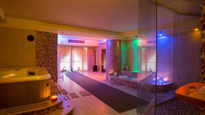 A spa area with a hot tub, a massage table, and a glass-enclosed shower.
