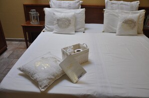 A neatly made bed with white linens and decorative pillows, a bedside table with a lantern, and a basket with a booklet.