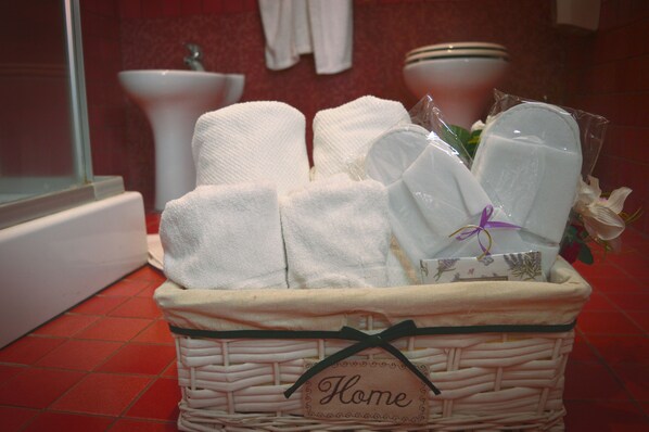 A wicker basket labeled "Home" containing white towels and a gift wrapped in white paper with a purple ribbon.