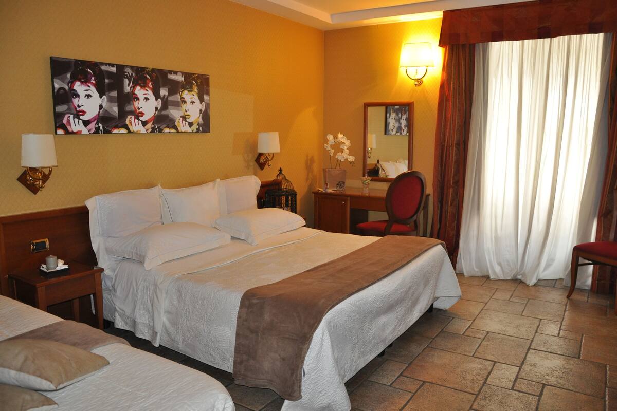 A hotel room with a large bed, a desk, a chair, and a painting on the wall.