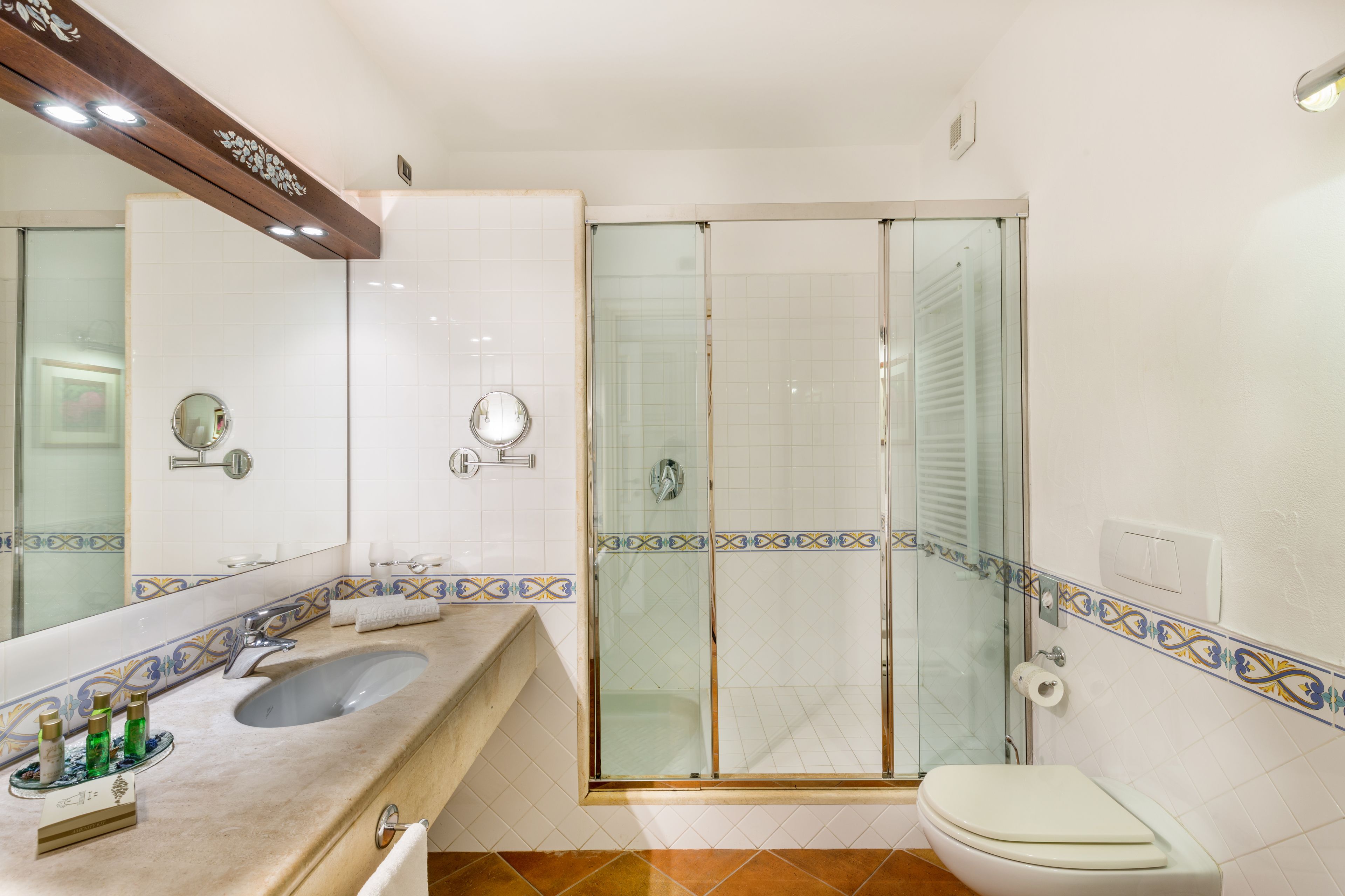 A bathroom with a sink, mirror, toilet, and glass shower enclosure.