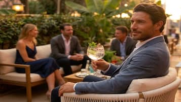 A man seated on a wicker chair outdoors, holding a drink.