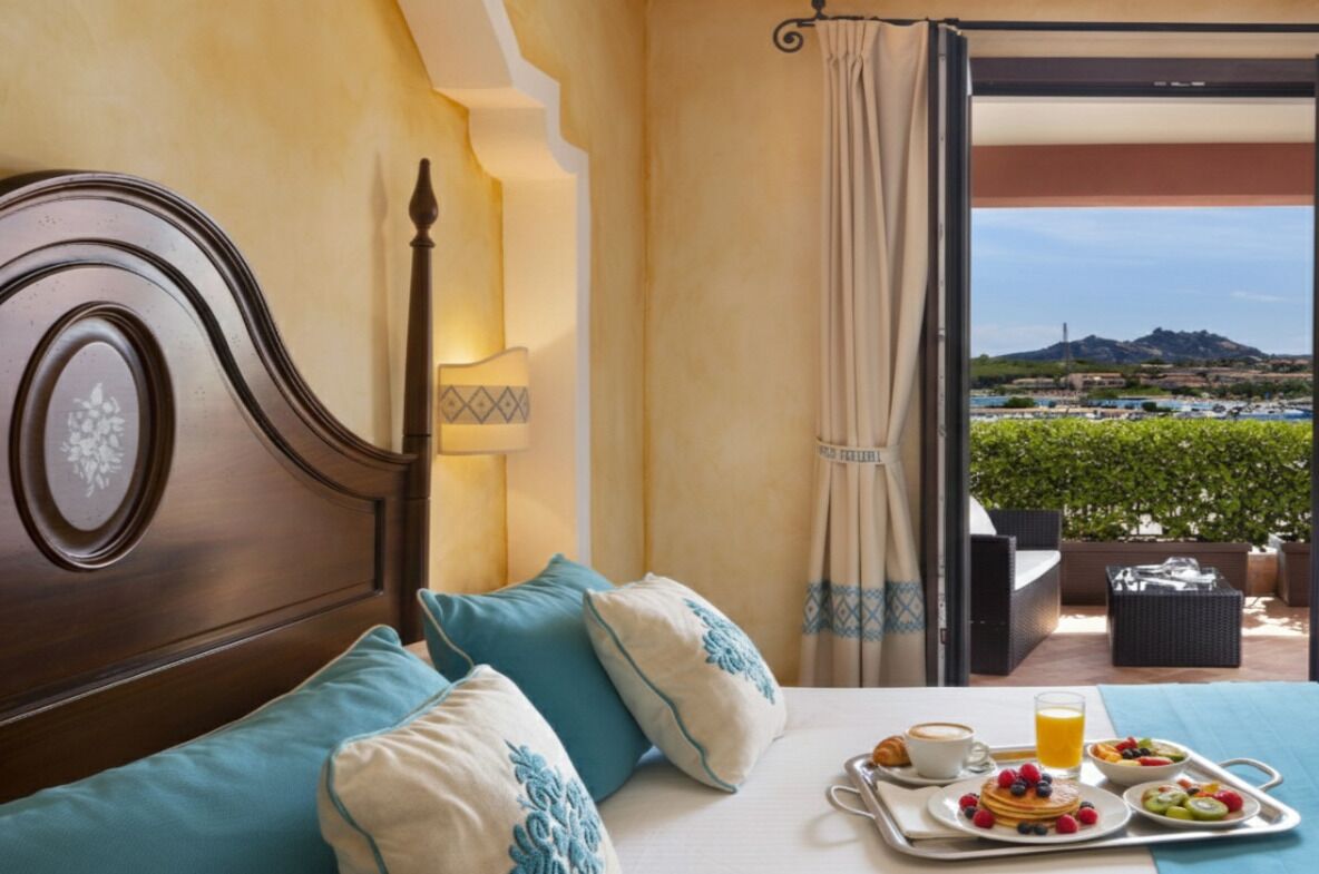 A hotel room with a bed, breakfast tray, and a view of a landscape.
