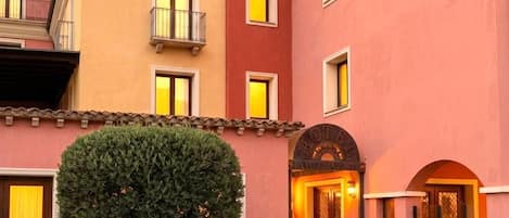 A multi-story hotel with a pink facade, balconies, and a tree in front.