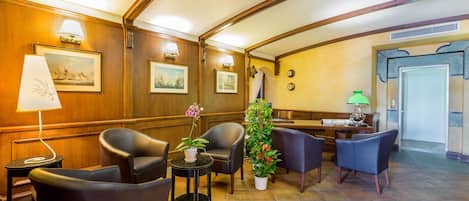 Un vestíbulo con paneles de madera, una mesa de recepción y varias zonas de estar con sillas y mesas.