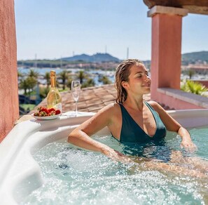 Una persona en un jacuzzi con una botella de champán y una copa, con vistas a un paisaje pintoresco.