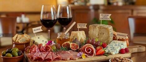 A charcuterie board with various cheeses, meats, and fruits, accompanied by two glasses of red wine.