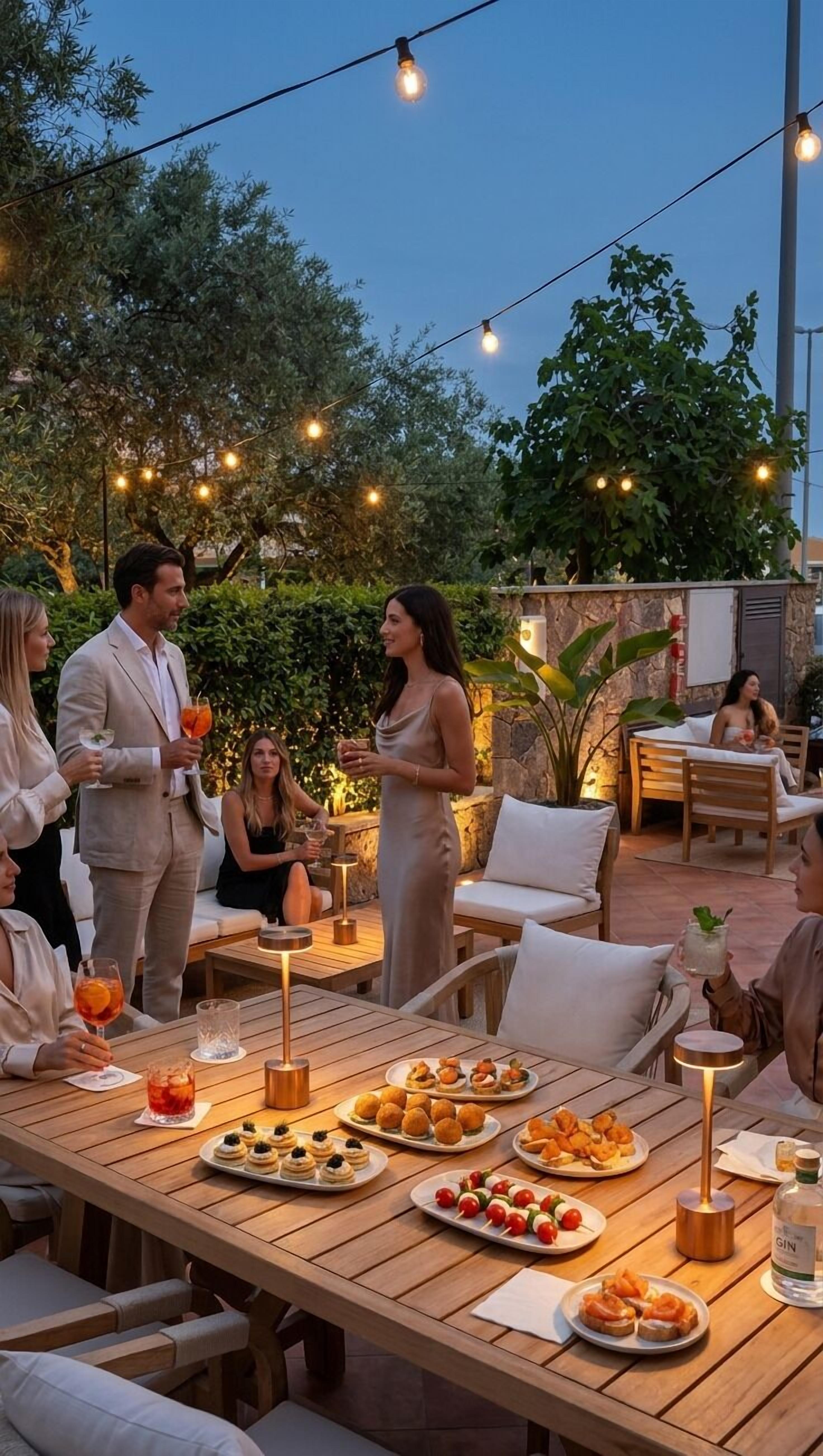 An outdoor dining area with string lights, wooden tables, and a variety of food and drinks.