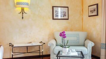 Une pièce avec un canapé de couleur claire, une petite table sur laquelle se trouvent une tasse et une soucoupe blanches, une orchidée en pot, une lampe fixée au mur et deux tableaux encadrés accrochés au mur.