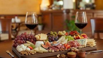 Una tabla de quesos y embutidos con varias variedades de queso, frutas y frutos secos, acompañada de dos copas de vino tinto sobre una mesa de madera.