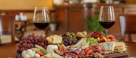 A charcuterie board with various cheeses, fruits, and nuts, accompanied by two glasses of red wine on a wooden table.