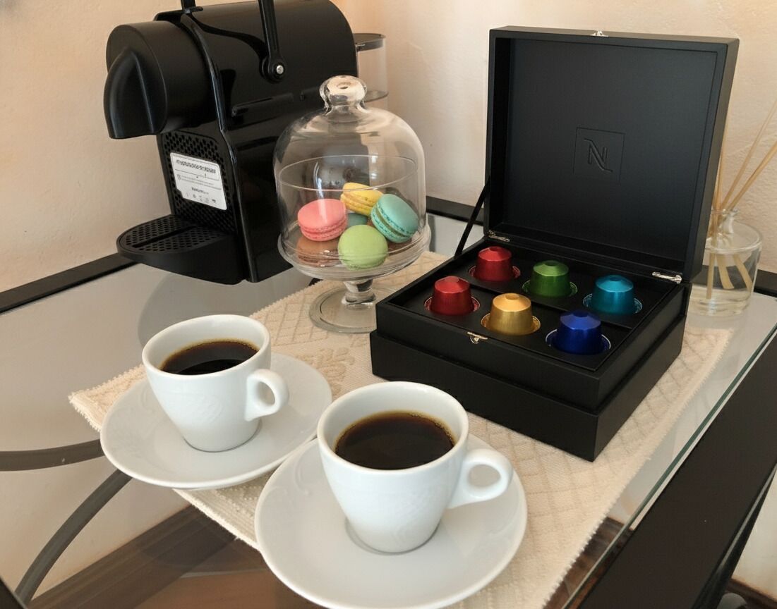 A coffee machine, two cups of coffee, a box of colorful macarons, and a glass container with a lid.