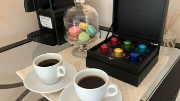 A coffee machine, two cups of coffee, a box of colorful macarons, and a glass container with a lid.