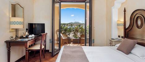 Habitación de hotel con cama, escritorio, silla, televisor y balcón con vistas.