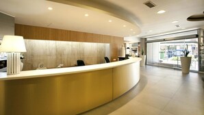 A modern reception area with a curved reception desk, a lamp, and a large potted plant. - Port Eugeni (Cambrils)