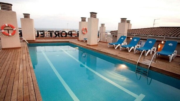 A pool area with blue water, wooden deck, and blue lounge chairs. - Port Eugeni (Cambrils)