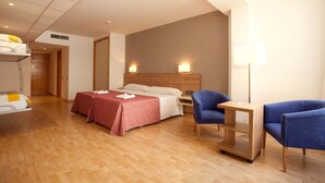 A hotel room with two beds, a desk, two chairs, a lamp, and a bedside table. - Port Eugeni (Cambrils)