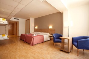A hotel room with two beds, a desk, two chairs, a lamp, and a bedside table. - Port Eugeni (Cambrils)