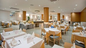 A spacious dining area with multiple tables and chairs, a central buffet, and a well-lit ceiling with recessed lighting. - Port Eugeni (Cambrils)