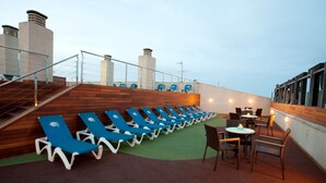 A deck with blue lounge chairs and a few tables, surrounded by a wooden wall and metal railings. - Port Eugeni (Cambrils)