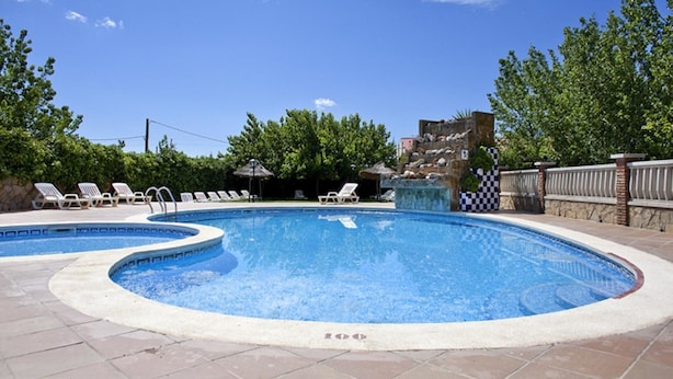 A swimming pool with two separate sections, surrounded by lounge chairs and a checkered fence. - Delta Hotel (Deltebre)