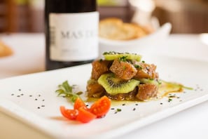 A dish with meat, kiwi, and cherry tomatoes on a white plate. - Delta Hotel (Deltebre)